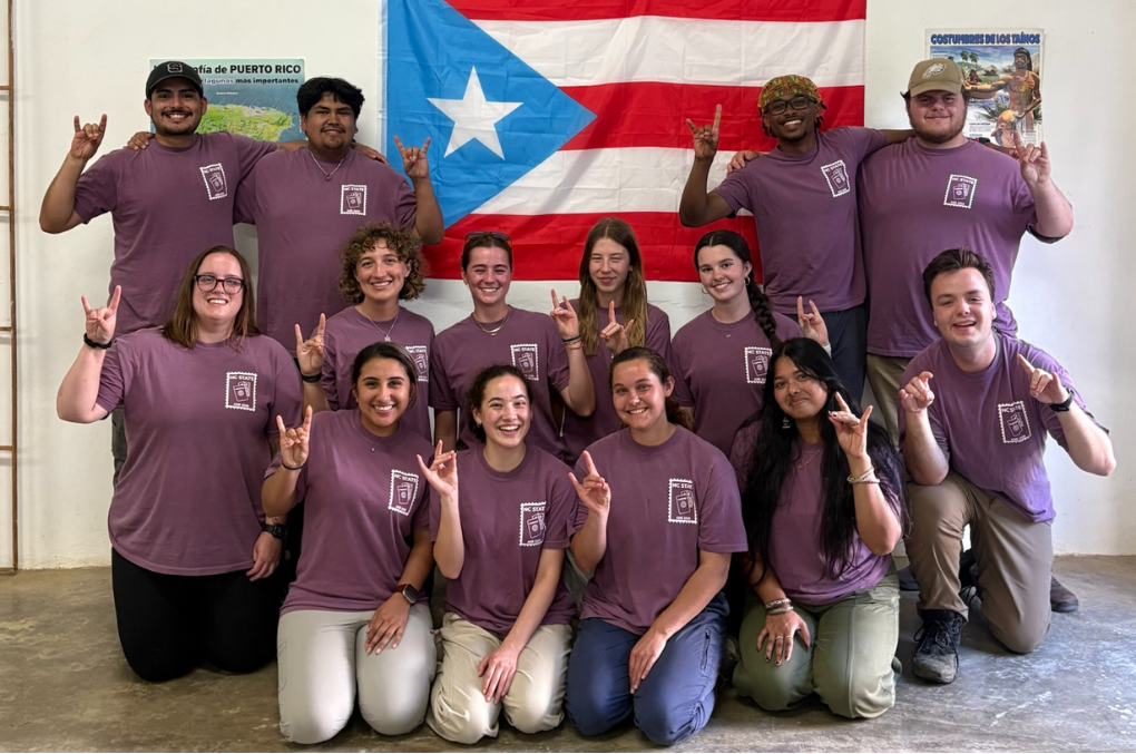 ASB Puerto Rico participants wearing a purple ASB t-shirt posing in front of a Puerto Rico flag.