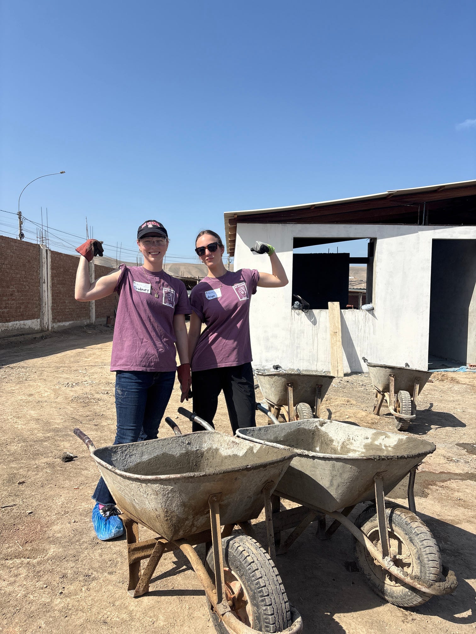 Two ASB Peru participants moving concrete in wheelbarrows at the service site.